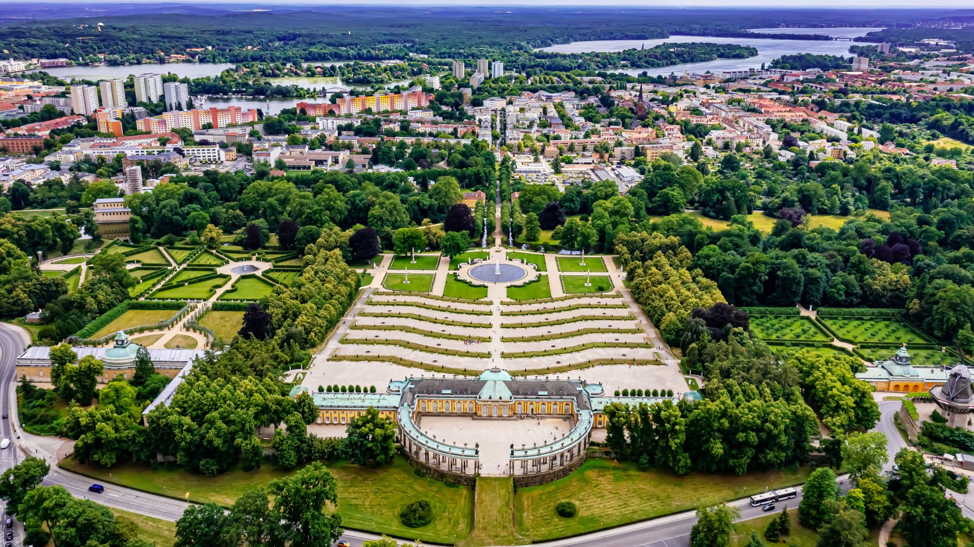Blick von oben &uuml;ber das Schloss Sanssouci mit Stadt und Seen im Hintergrund.